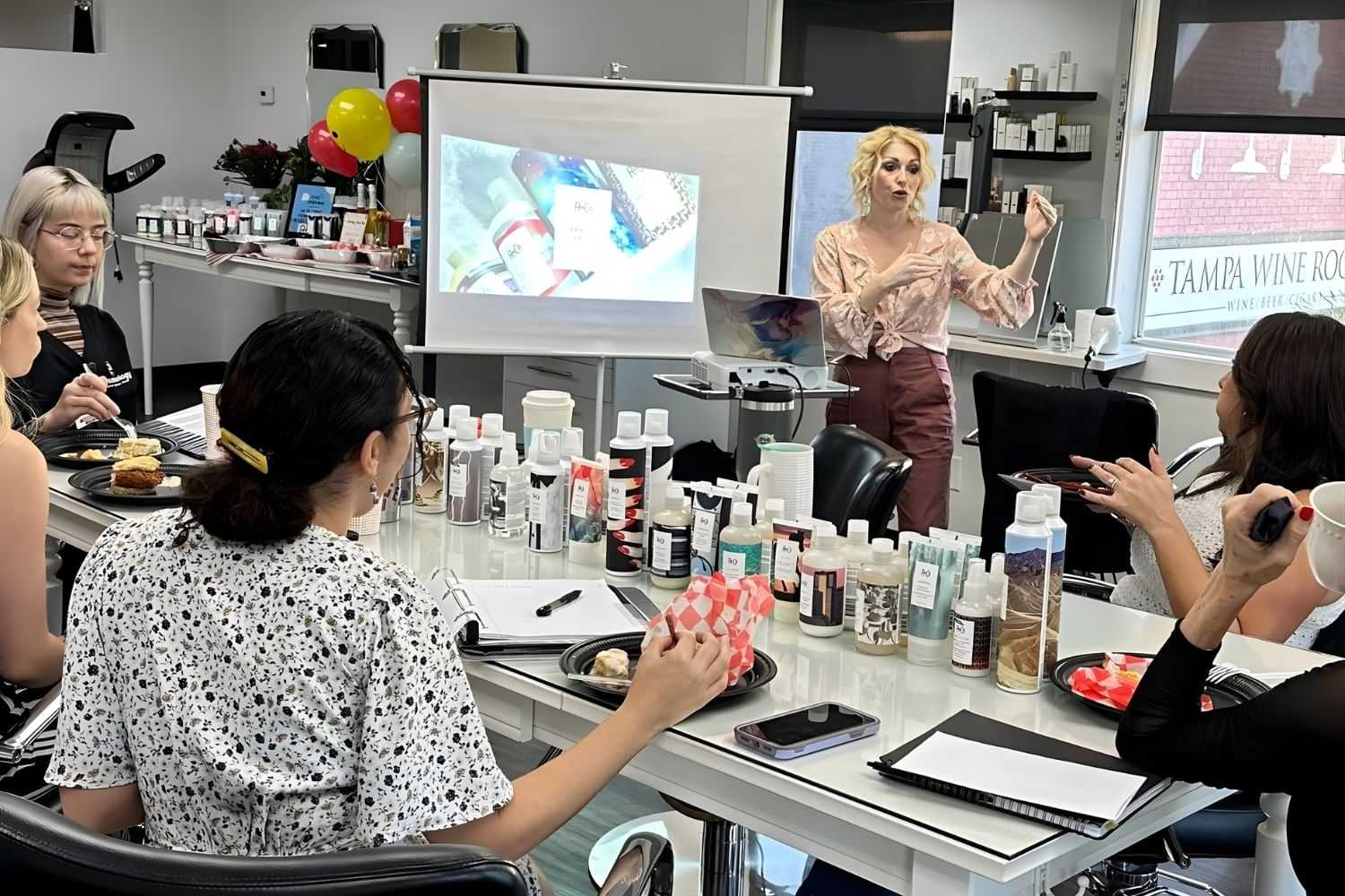 Beauty workshop with a presenter sharing tips, surrounded by an audience and various products.