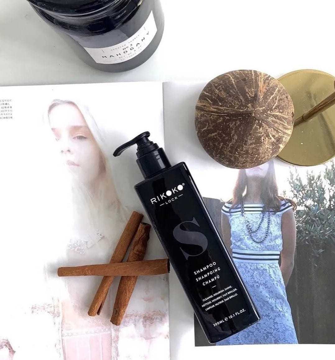 Shampoo bottle on fashion magazines with cinnamon sticks and candle nearby.