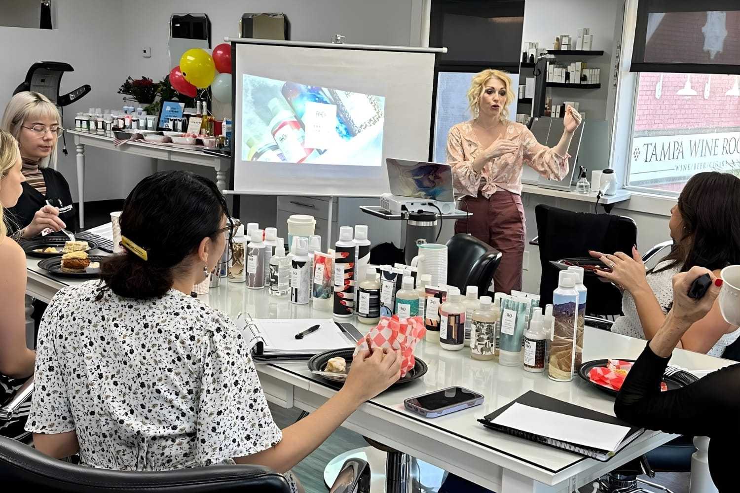 Beauty workshop with a presenter sharing tips, surrounded by an audience and various products.